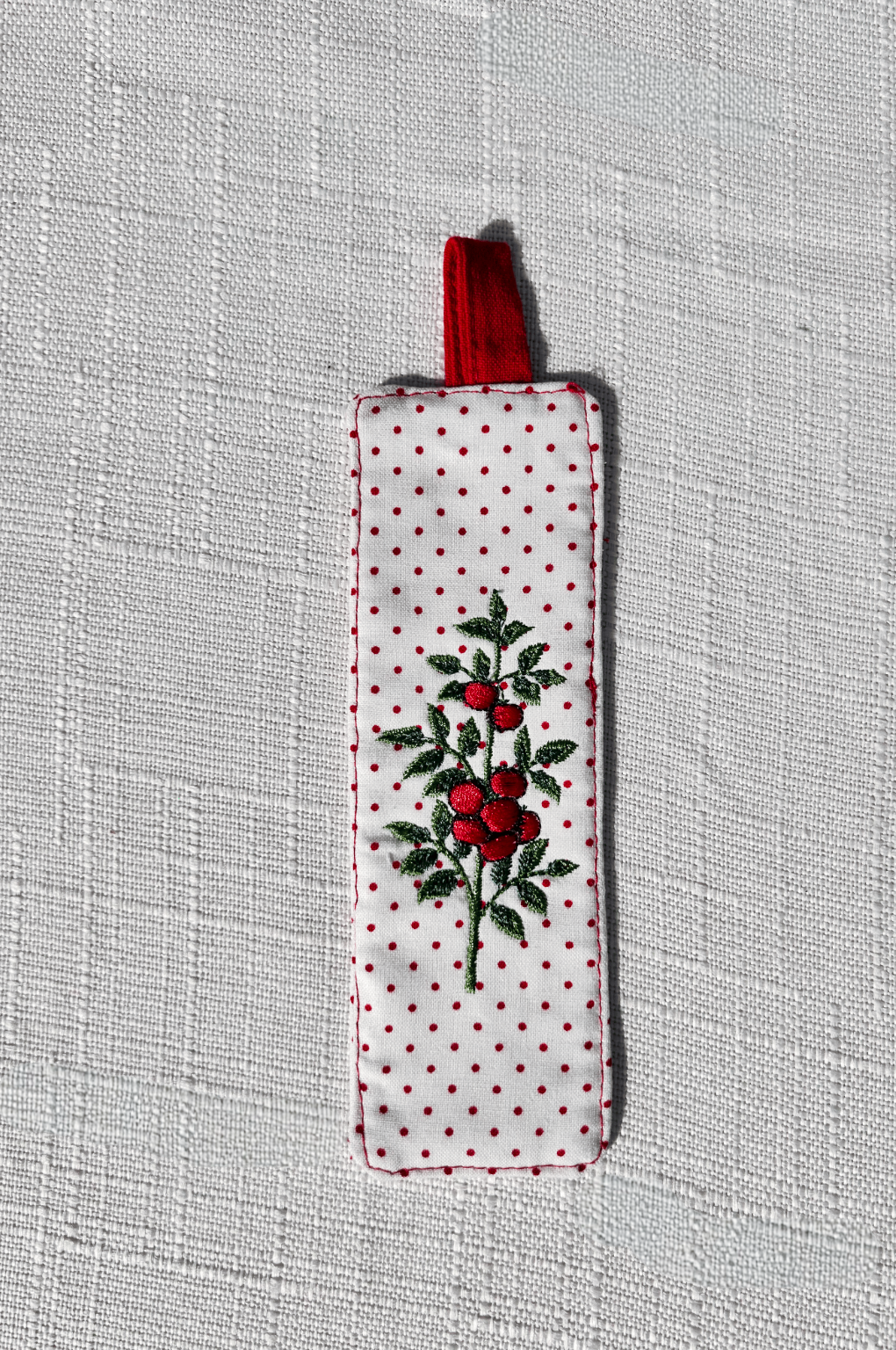Handsewn white fabric bookmark with small red polka dots and an embroidered tomato plant on both sides, finished with a red fabric loop at the top. perfect for cookbooks
