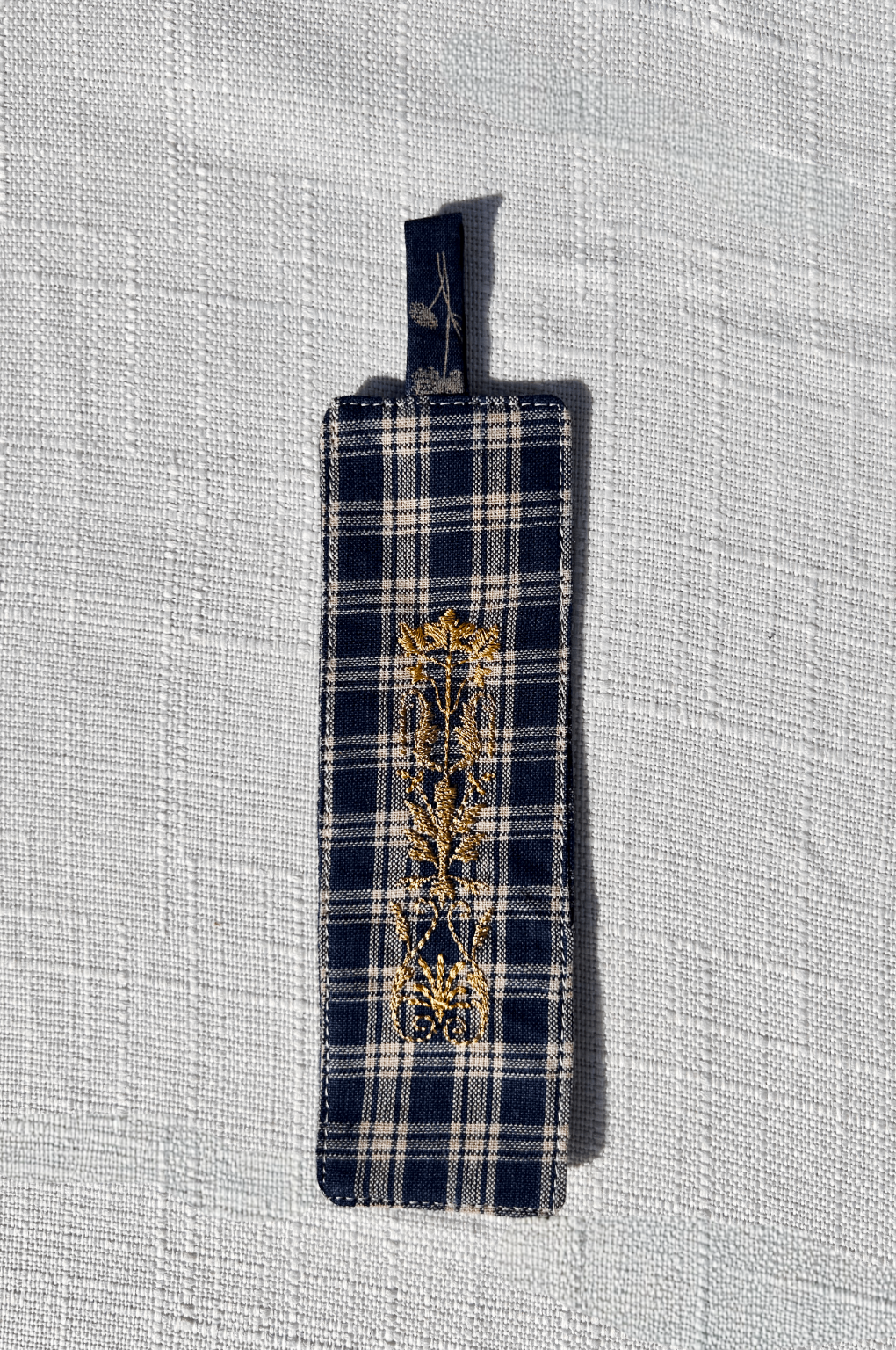 Navy and white plaid standard size fabric bookmark with tab with golden crest embroidery on the front and back . a part of a matching set with a glasses case