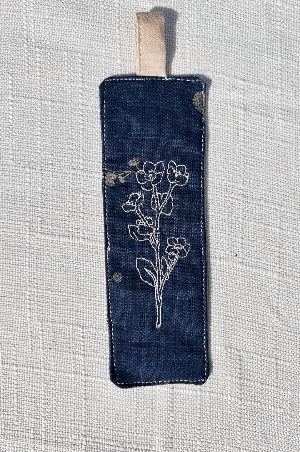 Navy blue  floral cotton handmade bookmark with floral  line art embroidered on the  front and back and an extended tab in tan 